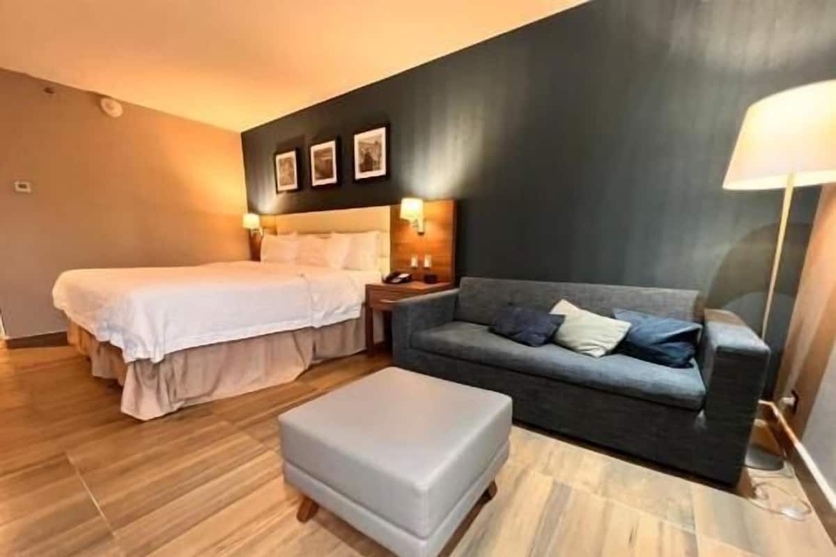 A hotel room with a bed, a sofa, a nightstand, and a lamp.