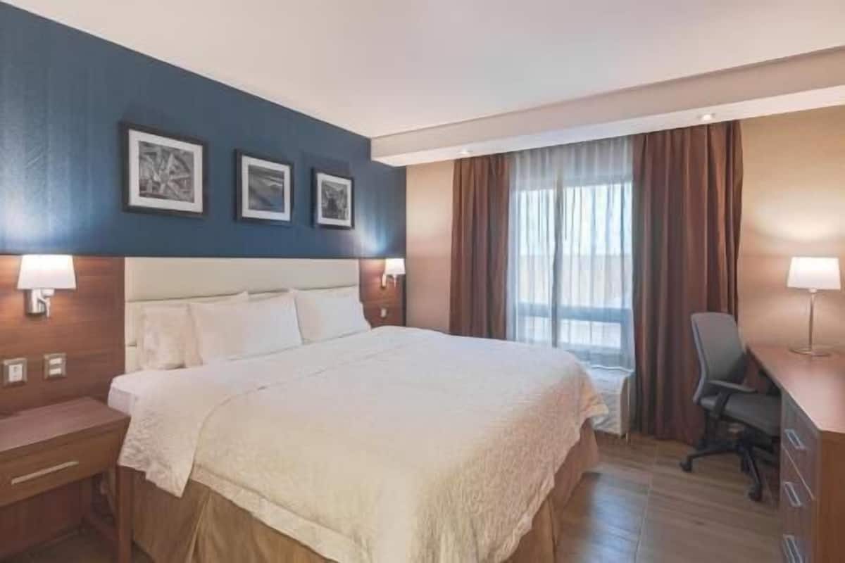 A hotel room with a large bed, bedside tables, a desk, and a window with curtains.