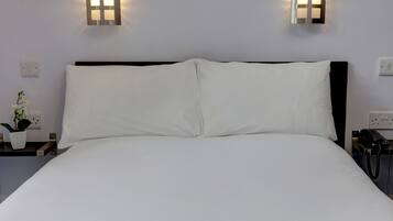 A neatly made bed with white linens, two wall-mounted light fixtures, a bedside table with a plant, and a phone on a stand.