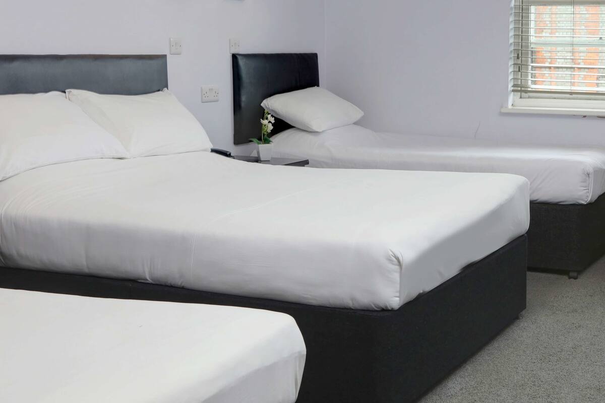 Hotellihuone, jossa on kaksi sänkyä, yöpöytä, pieni pöytä ja ikkuna, jossa on sälekaihtimet.