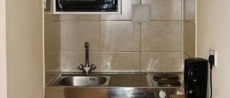 A compact kitchen with a microwave, stove, sink, and a coffee maker on a small countertop.