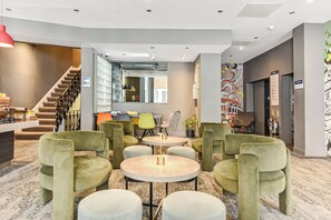 A lobby with a staircase, seating area, and a wall with a mural. - Heeton Concept Hotel Kensington (London)