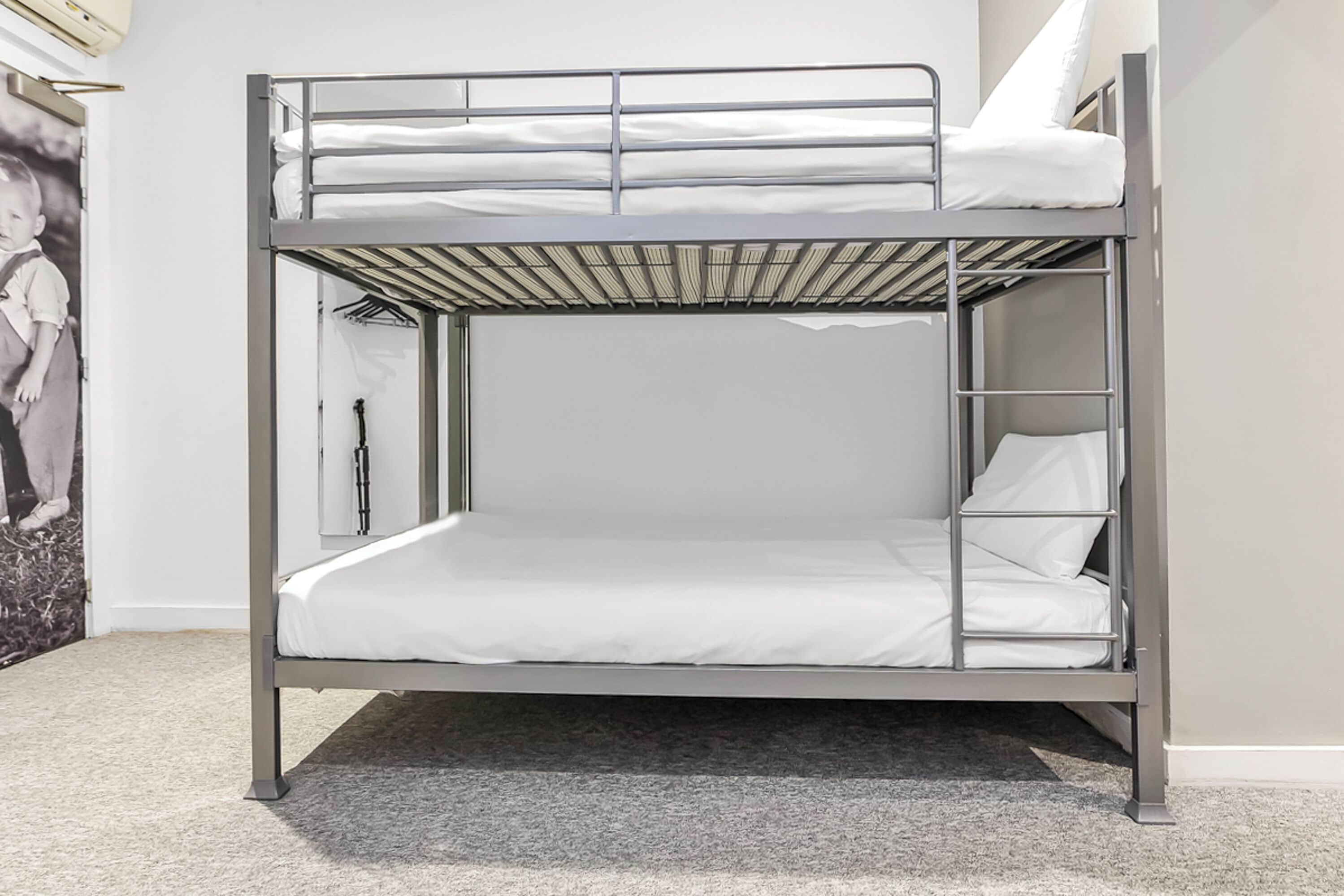Ein Etagenbett mit Metallgestell, weißer Bettwäsche und einem kleinen Ablagefach an der Seite.