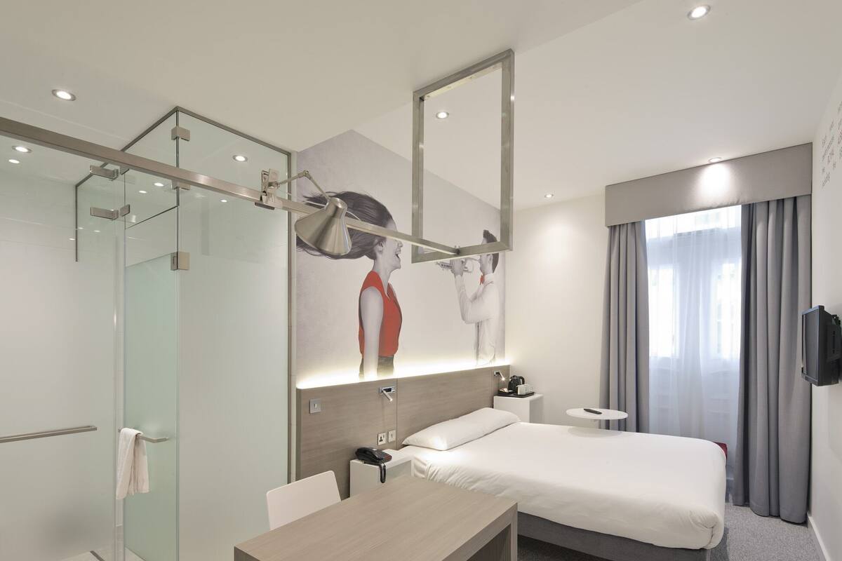 Een moderne hotelkamer met een bed, bureau en een douchecabine van glas.