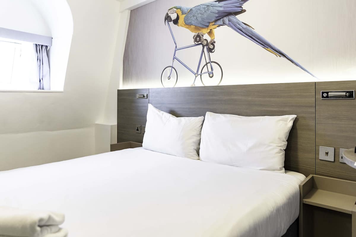 Een hotelkamer met een groot bed, een nachtkastje en een op de muur gemonteerde lichtschakelaar.