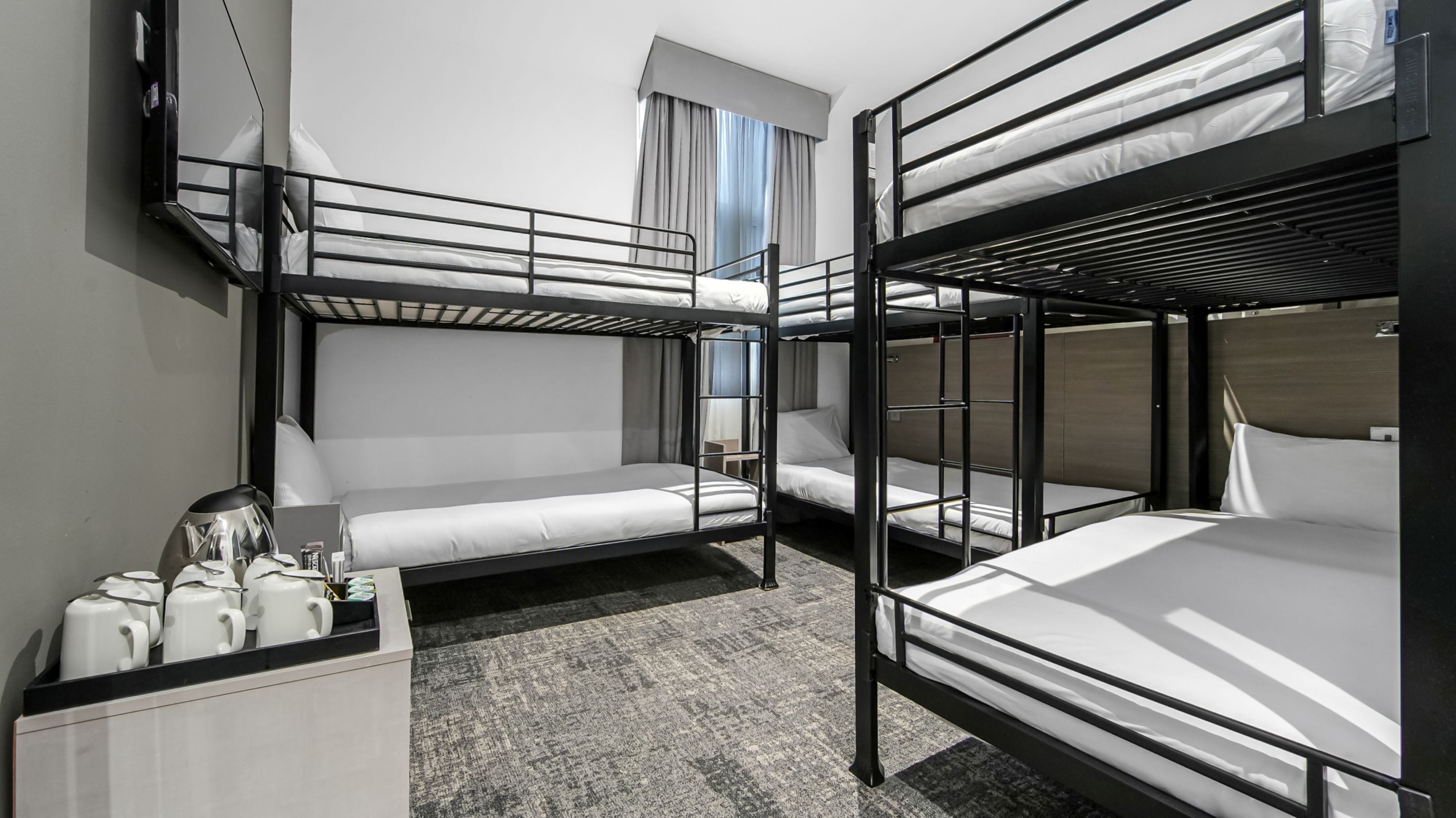 A bunk bed room with a desk, a coffee maker, and a window with curtains.
