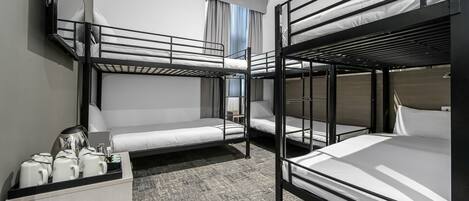 A bunk bed room with a desk, a coffee maker, and a window with curtains.