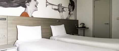 Habitación de hotel con dos camas, cabecera de madera, mesita de noche pequeña con lámpara y un cuadro en la pared que muestra a una persona tocando una trompeta.