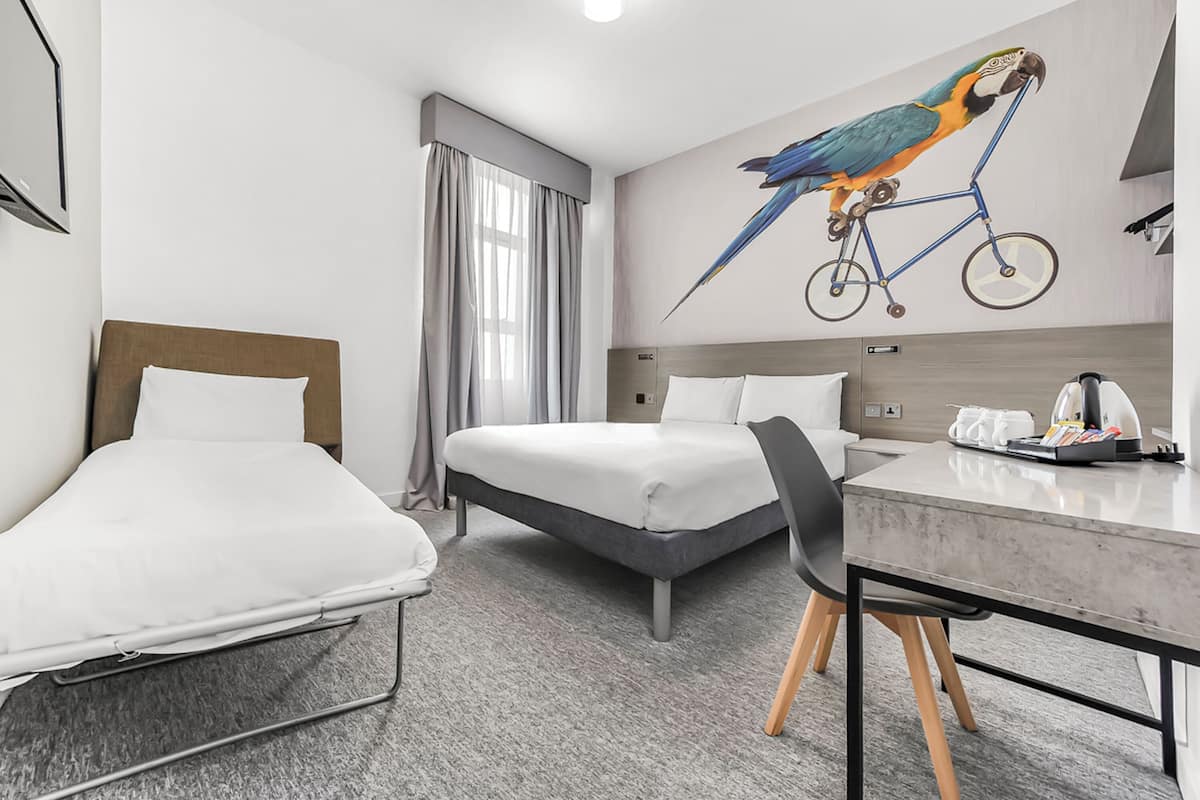 Een hotelkamer met twee eenpersoonsbedden, een bureau met een stoel, een koffiezetapparaat en een aan de muur bevestigde fiets.