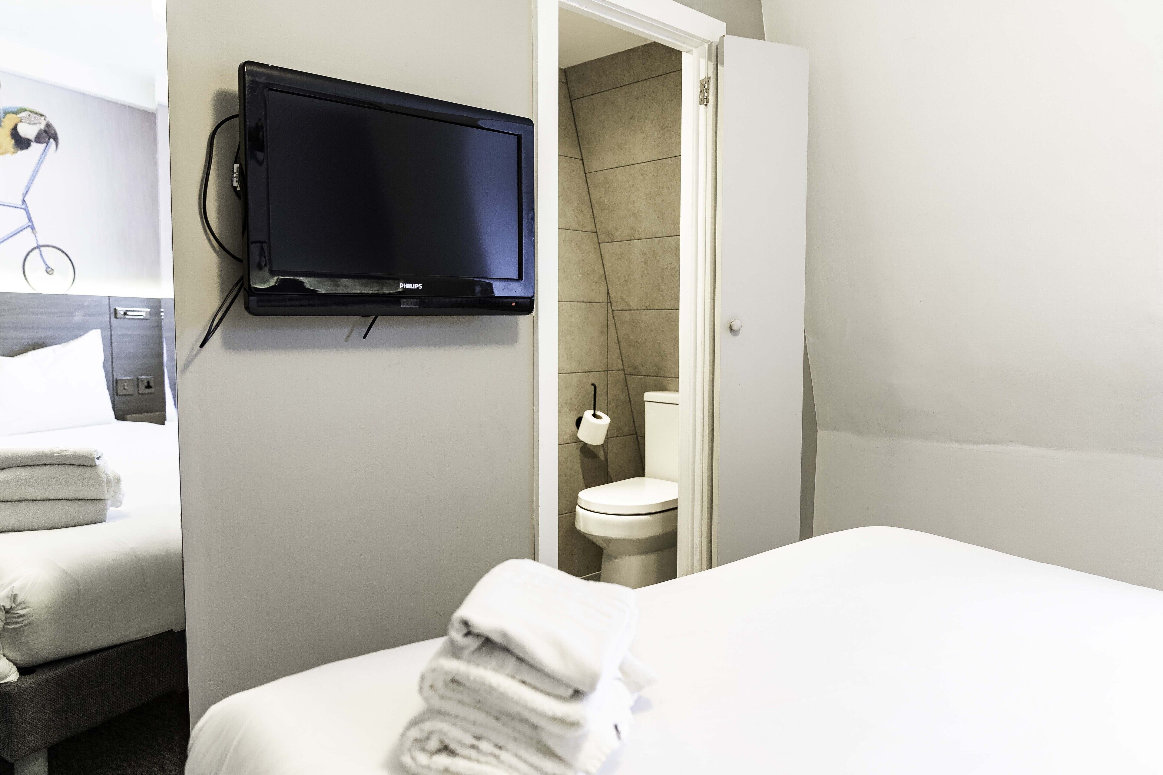 A hotel room with a bed, a TV mounted on the wall, and a bathroom visible through an open door.