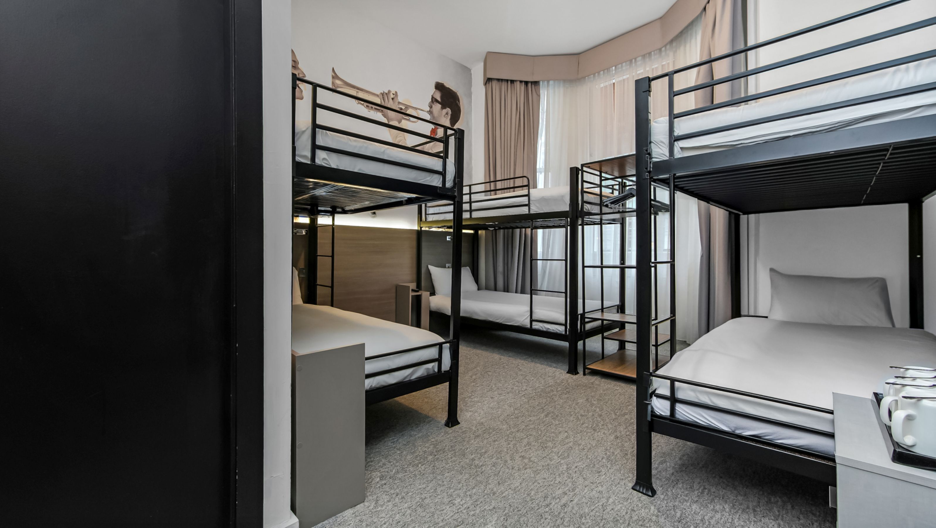 Een slaapkamer met stapelbed, bureau en stoel, een raam met gordijnen en een muur met een muurschildering.