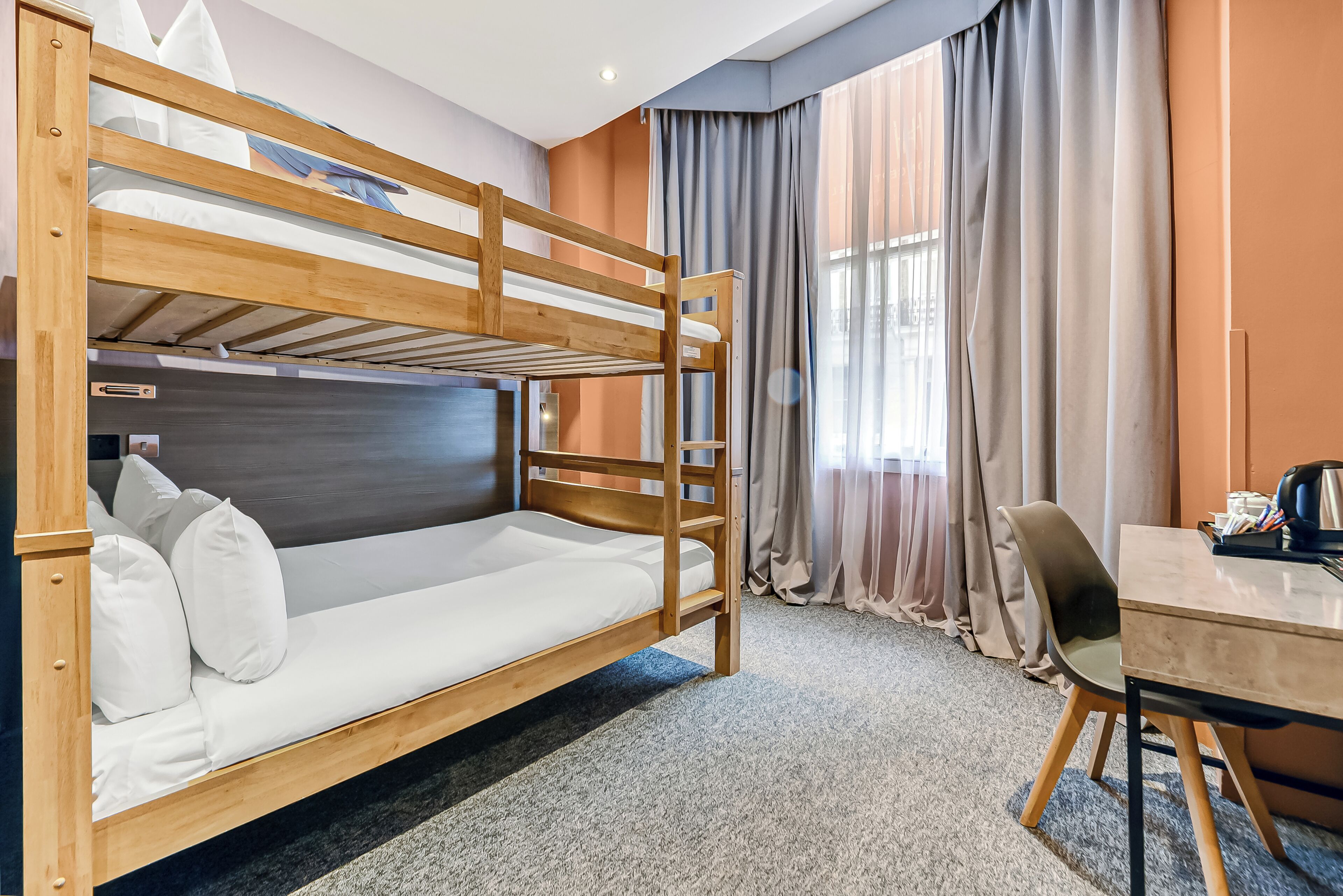 Una cama litera con escritorio, silla, cortinas y una ventana.