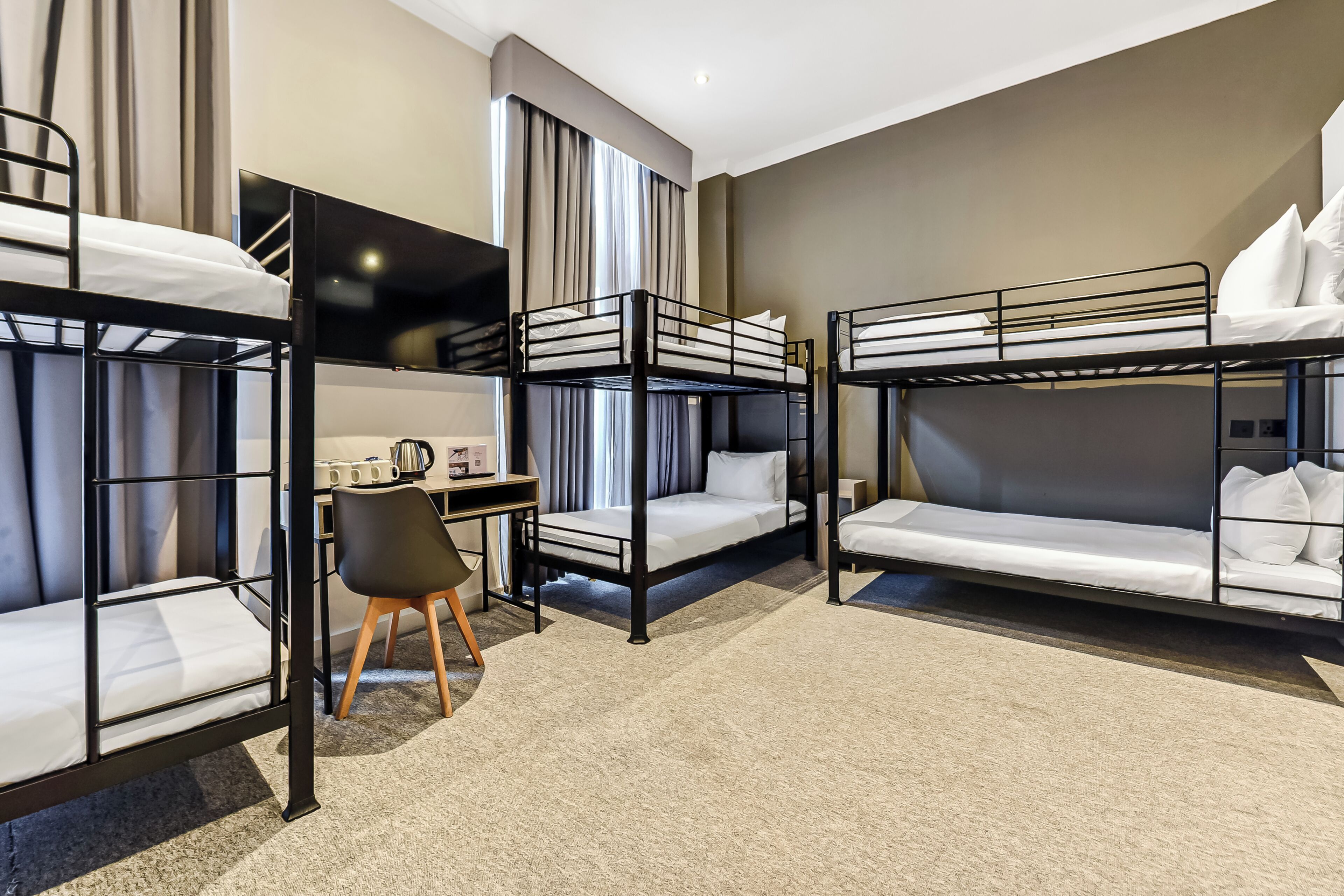 A hotel room with bunk beds, a desk, a chair, and a TV.