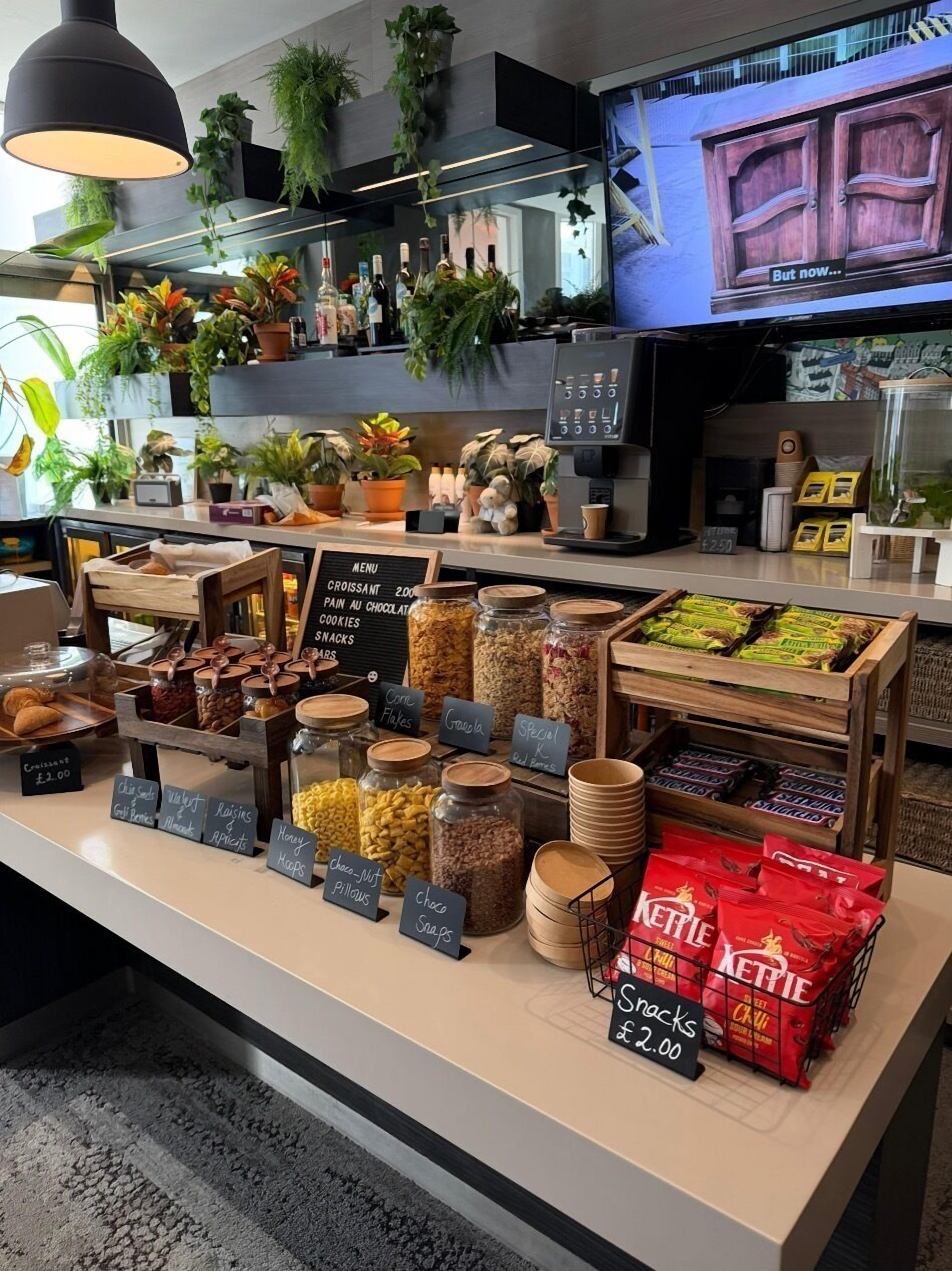 A bakery display with various baked goods and snacks, including jars of honey, chocolate, and nuts, and a selection of Kettle brand snacks.