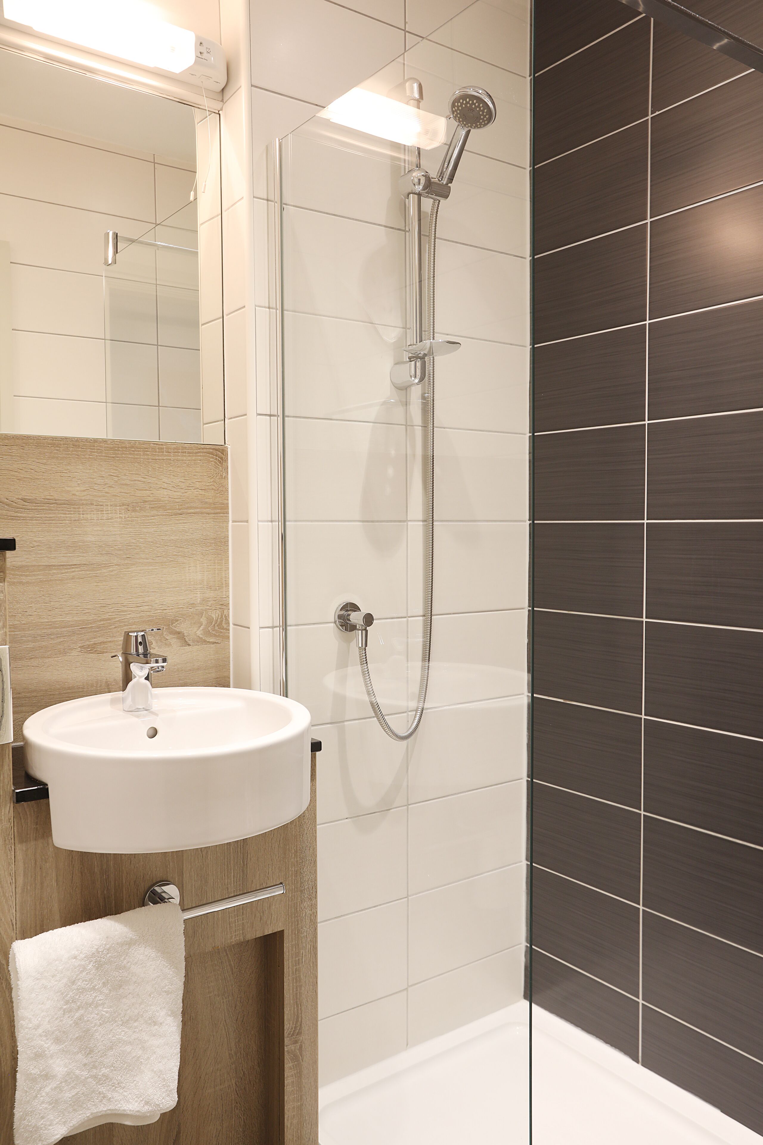 A modern bathroom with a glass-enclosed shower, a white sink, and a wooden vanity.