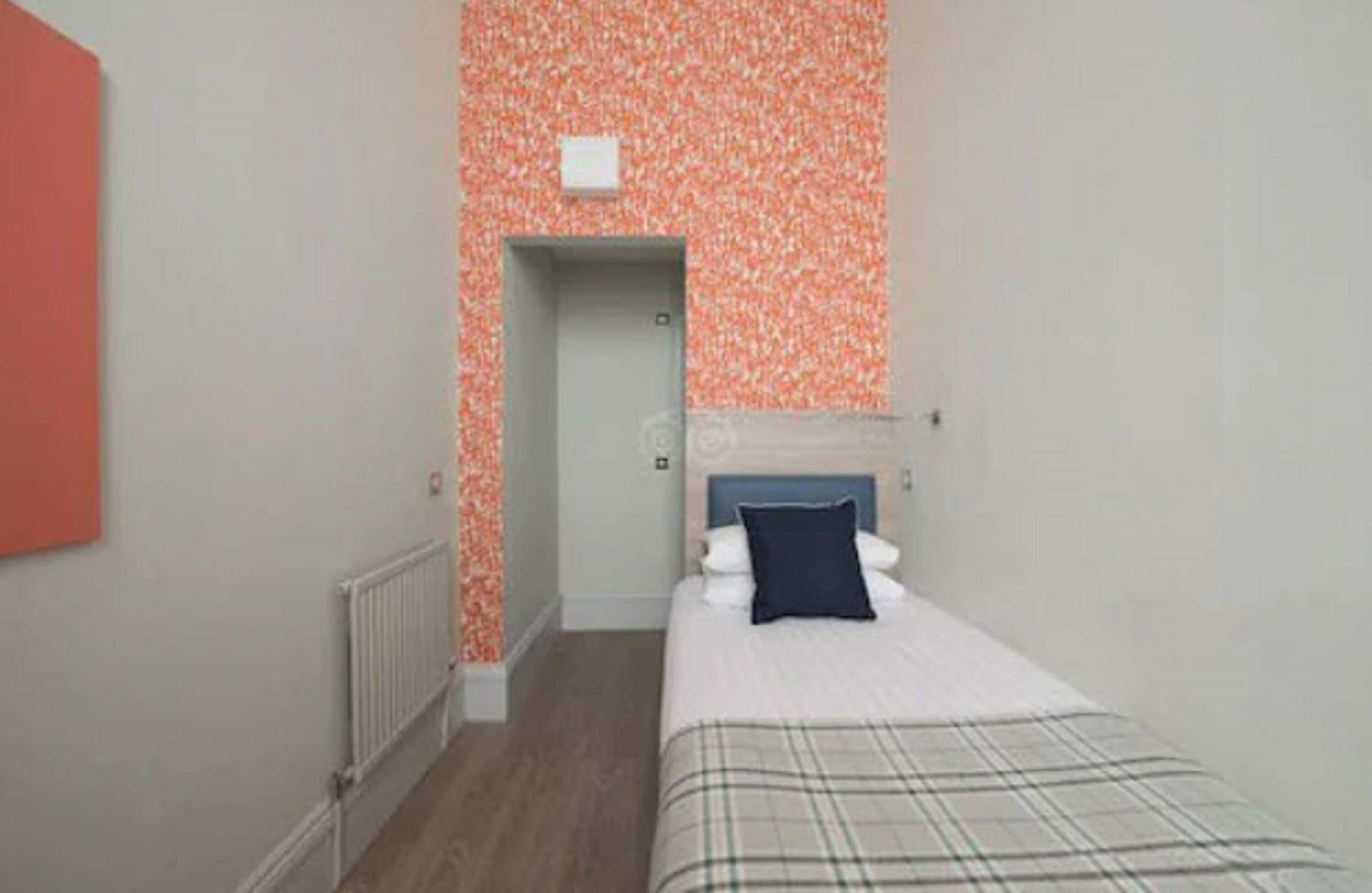 A bedroom with a bed, a headboard, a radiator, and a door leading to another room.