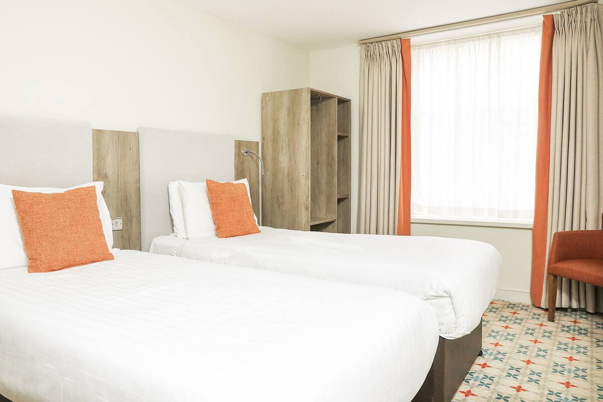 Ett hotellrum med två sängar, en garderob, en stol och ett fönster med gardiner.