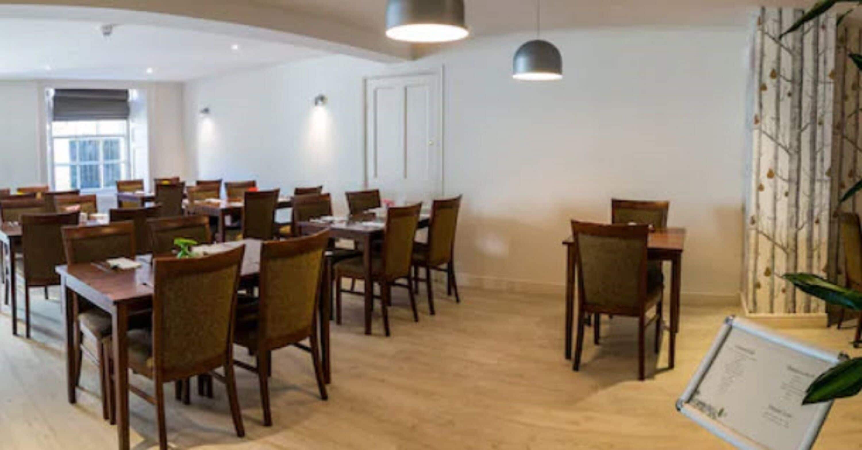 Un comedor con varias mesas y sillas, suelo de madera y una pared con jardín vertical.