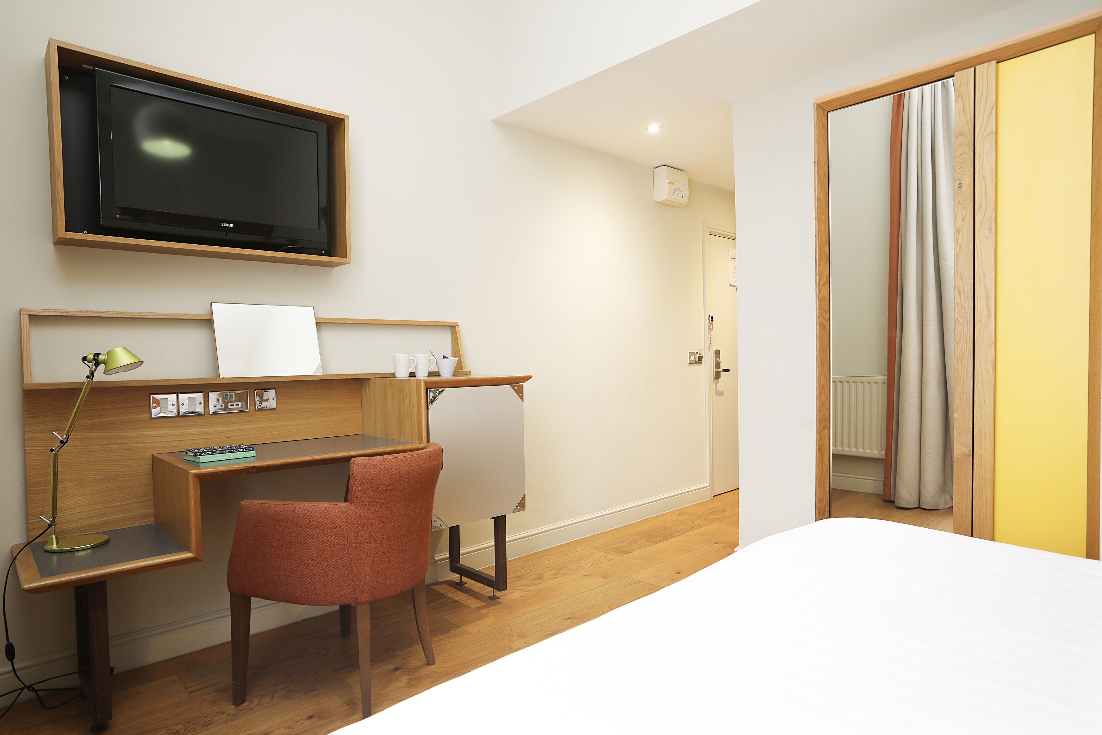 Una habitación de hotel con una cama, un escritorio con una silla, un televisor montado en la pared y una puerta que da a un baño.