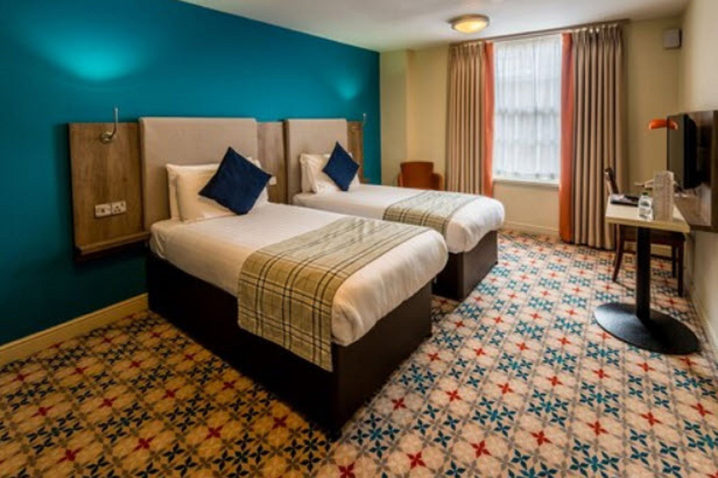 A hotel room with two beds, a television, a desk, and a window with curtains.