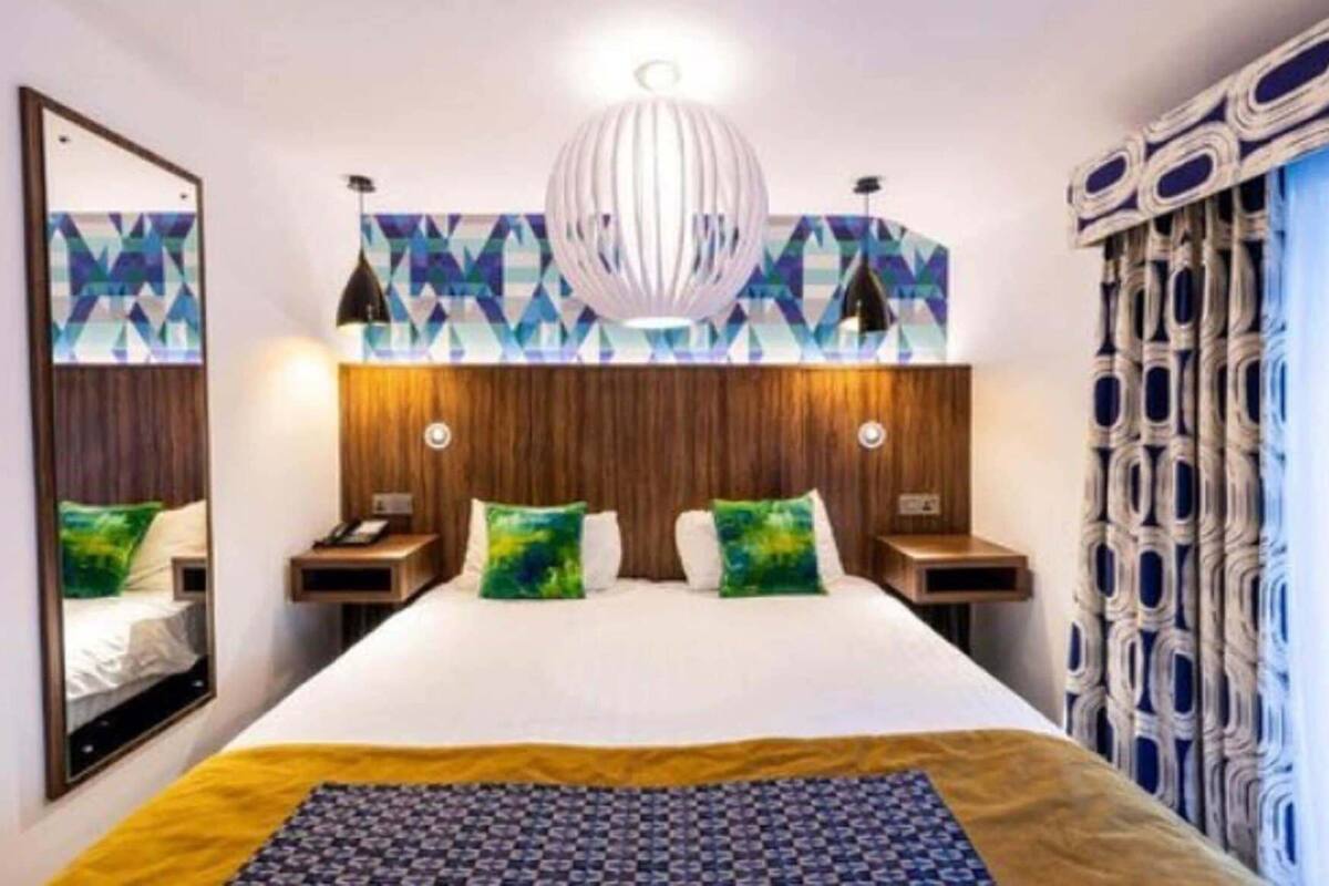 Ett hotellrum med en stor säng, ett träfärgat sänggavel, en spegel, en vägg med mönster och en dekorativ hängande lampa.