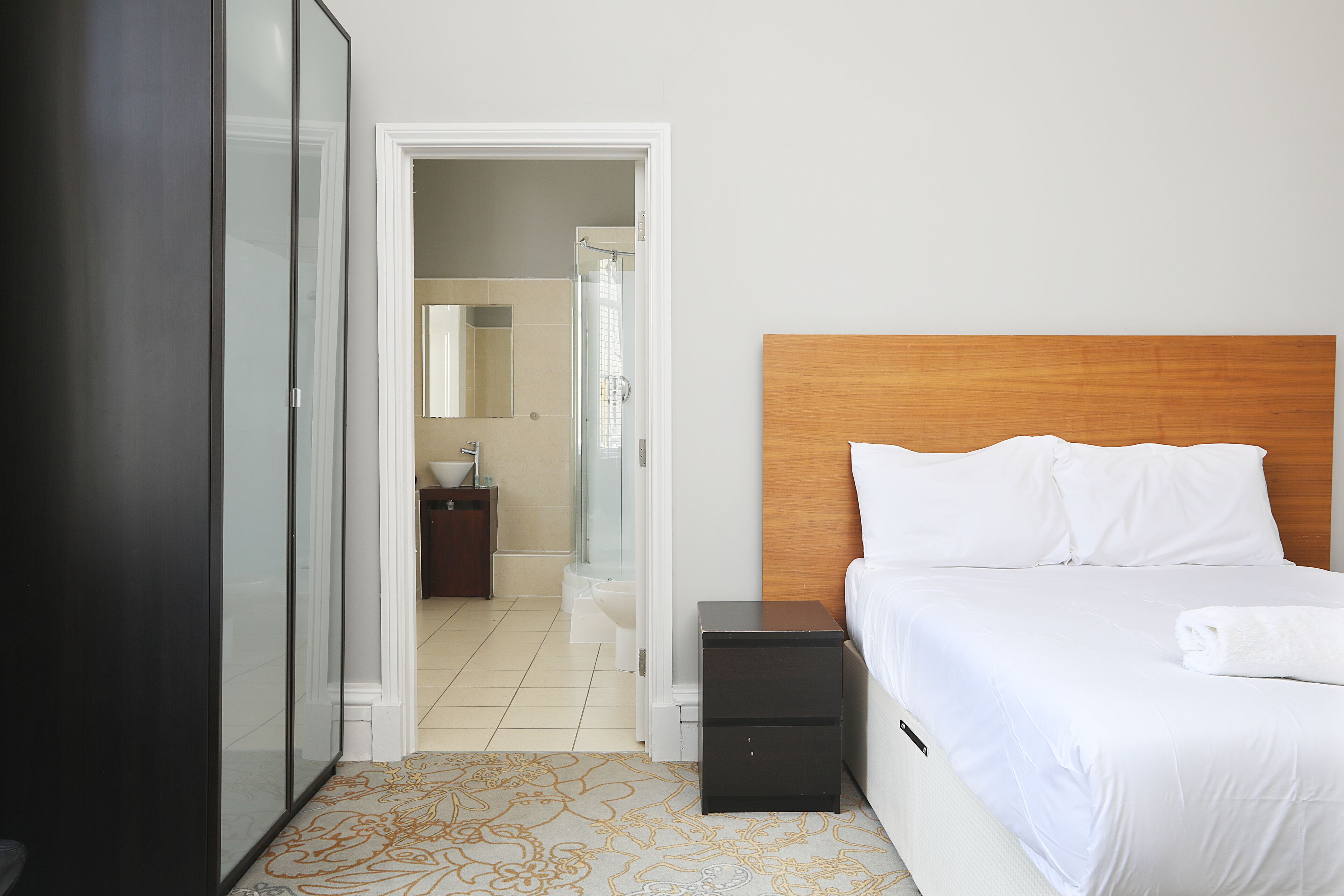 A hotel room with a bed, bedside tables, a wardrobe, and a bathroom visible through an open door.