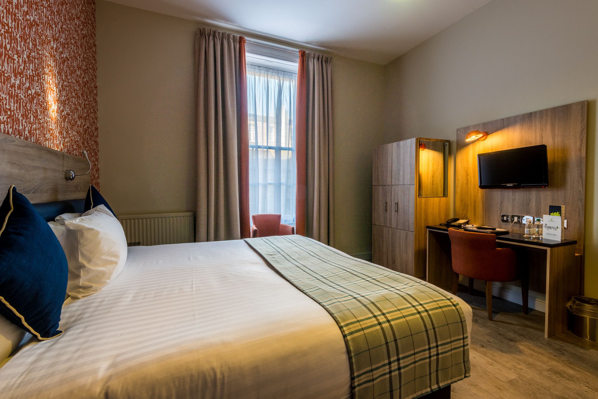 Une chambre d’hôtel avec un lit, un bureau, une chaise, une télévision et une fenêtre avec des rideaux.