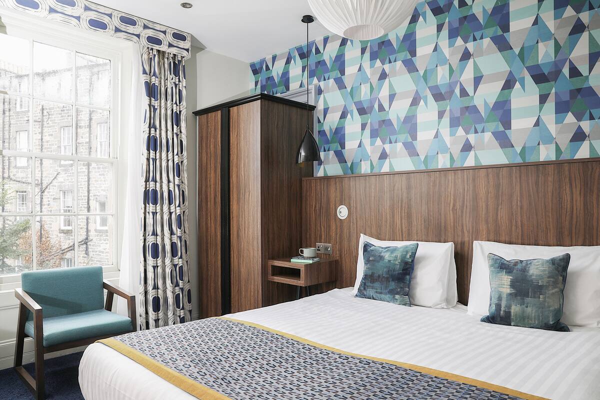 Ett hotellrum med en stor säng, en garderob i trä, en stol och utsikt över staden genom ett fönster.