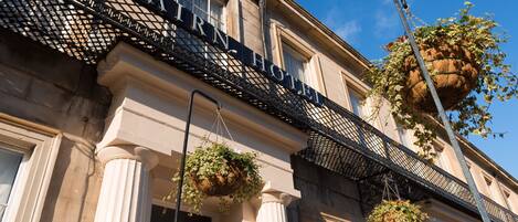 A hotel facade with a wrought iron sign reading "CARNIVAL HOTEL" and hanging flower baskets.