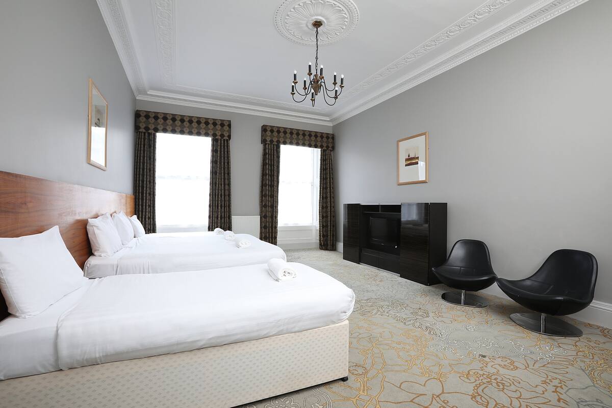 Ett hotellrum med en stor säng, två svarta stolar, en tv och en kristallkrona.