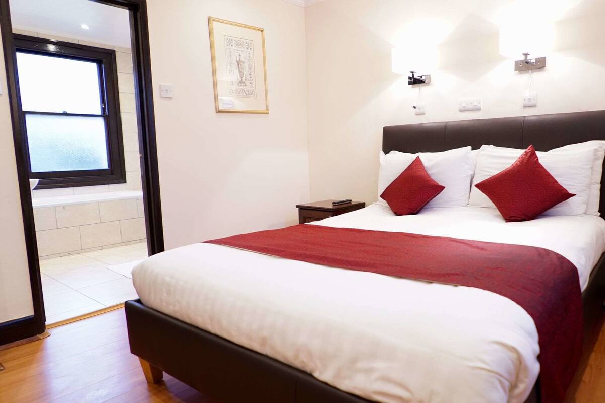 A hotel room with a bed, a nightstand, a window, and a door.