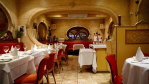Un restaurante con mesas dispuestas para comer, con una decoración clásica que incluye arcos y un ventanal decorativo central.