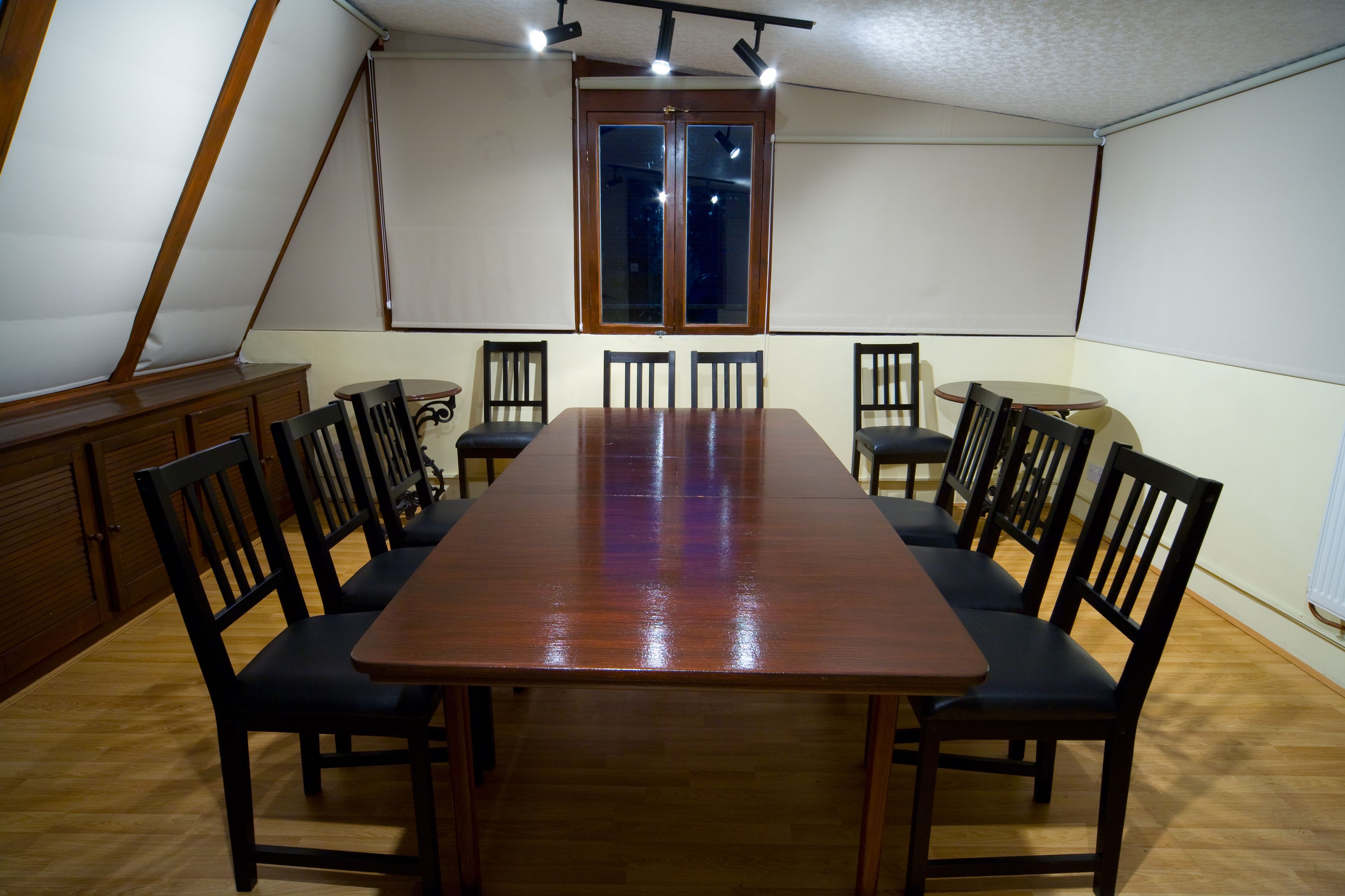 A conference room with a long wooden table, black chairs, a projector screen, and a window with blinds.