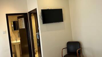 Ein Hotelzimmer mit einem Bett, einem Sessel, einem Fernseher, einem Deckenventilator und einem durch eine offene Tür einsehbaren Badezimmer.
