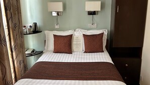 Habitación de hotel con una cama grande, dos lámparas de noche, una mesita de noche con hervidor y un armario.