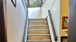 Una escalera de madera con barandilla que lleva a un rellano con un radiador y un cuadro en la pared.