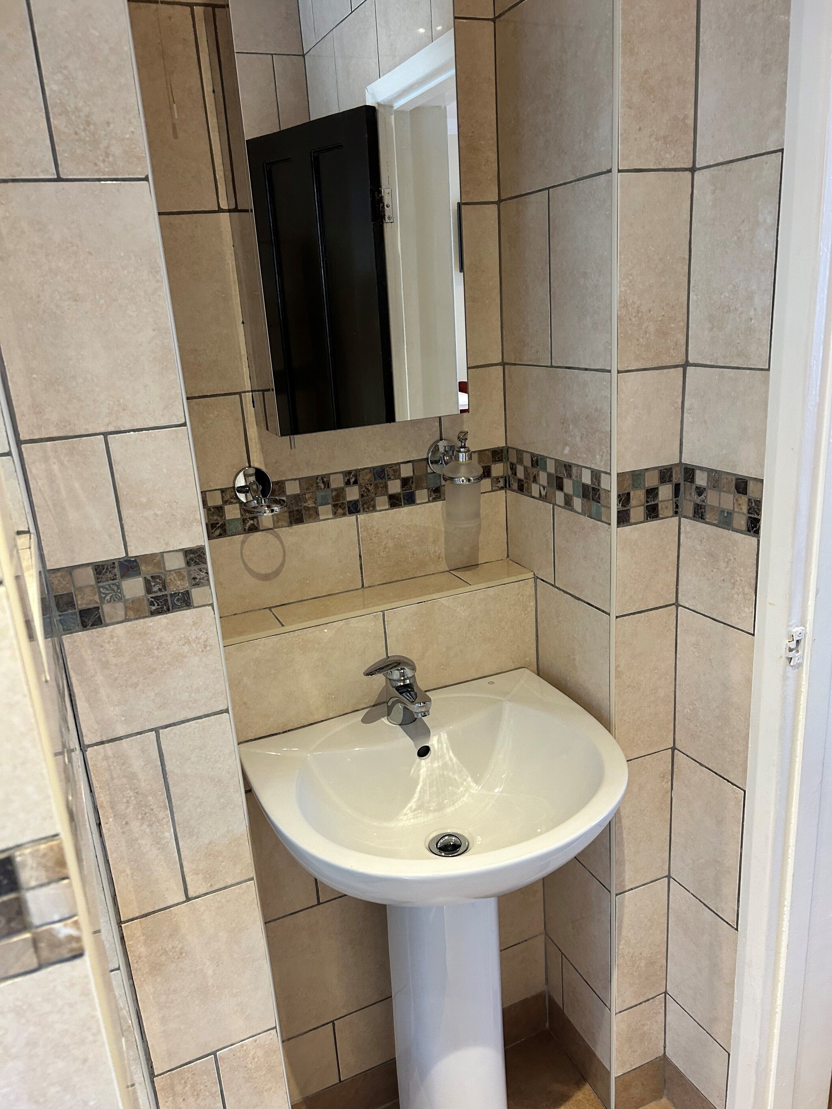 Un baño con un lavamanos pedestal blanco, un espejo encima y paredes con azulejos.