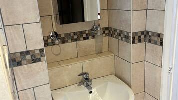 Une salle de bain avec un lavabo sur colonne blanc, un miroir au-dessus et des murs carrelés.