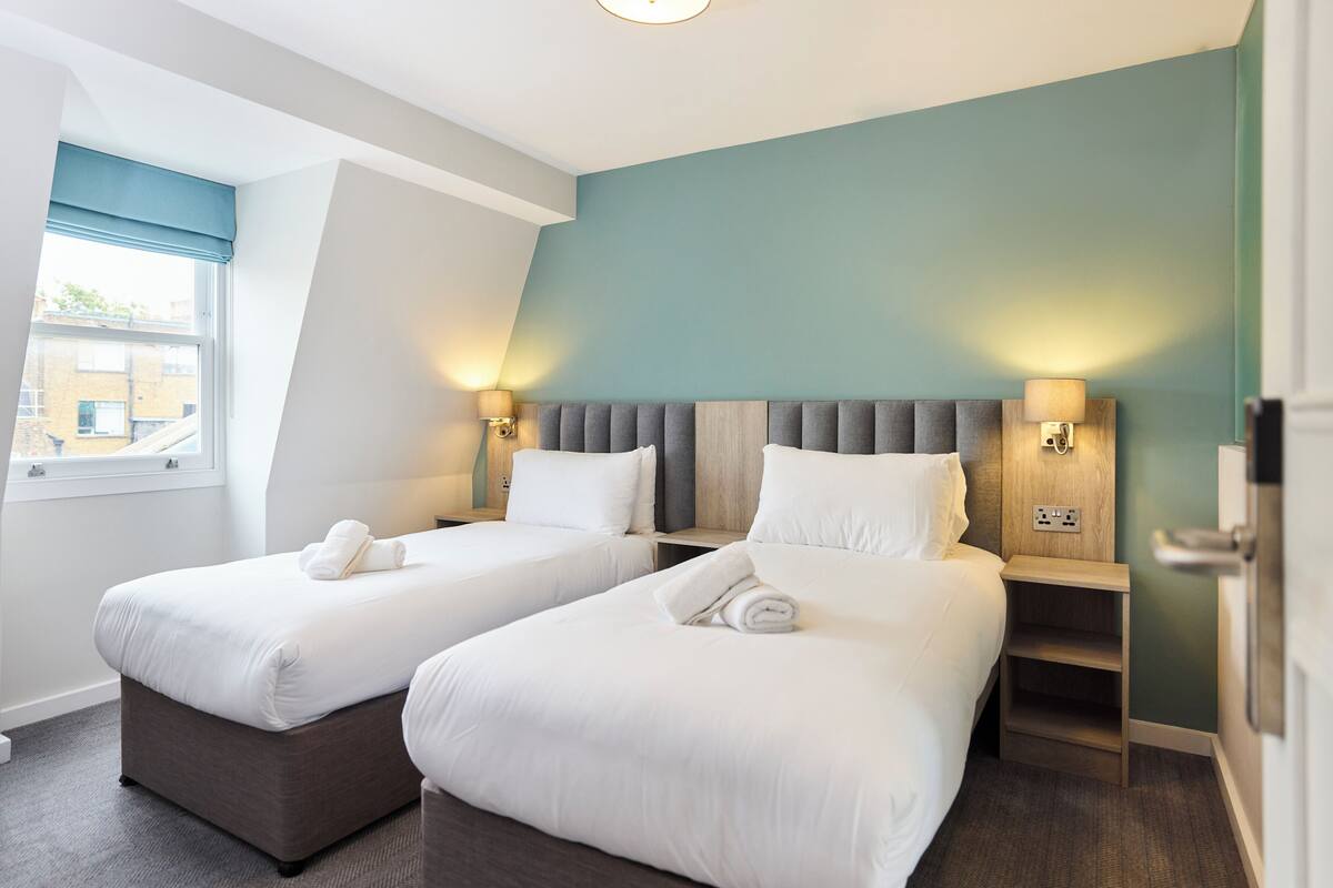A hotel room with two beds, a window with a view, and a nightstand with a lamp.