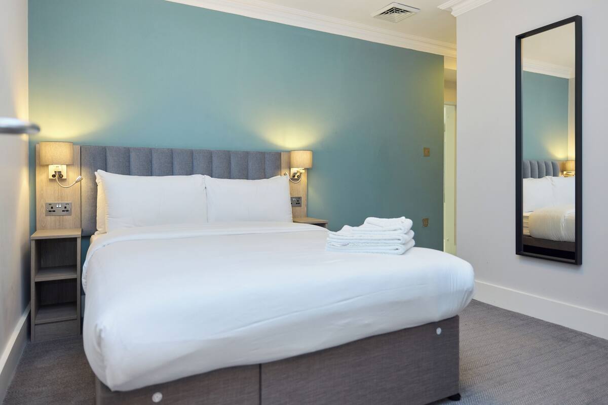 A neatly made bed with white linens, two bedside lamps, and a large mirror on the wall.