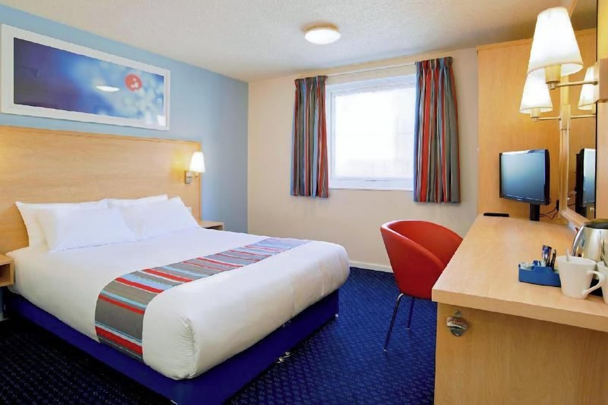 Une chambre d’hôtel équipée d’un lit, d’un bureau, d’une chaise, d’une télévision et d’une fenêtre avec des rideaux.