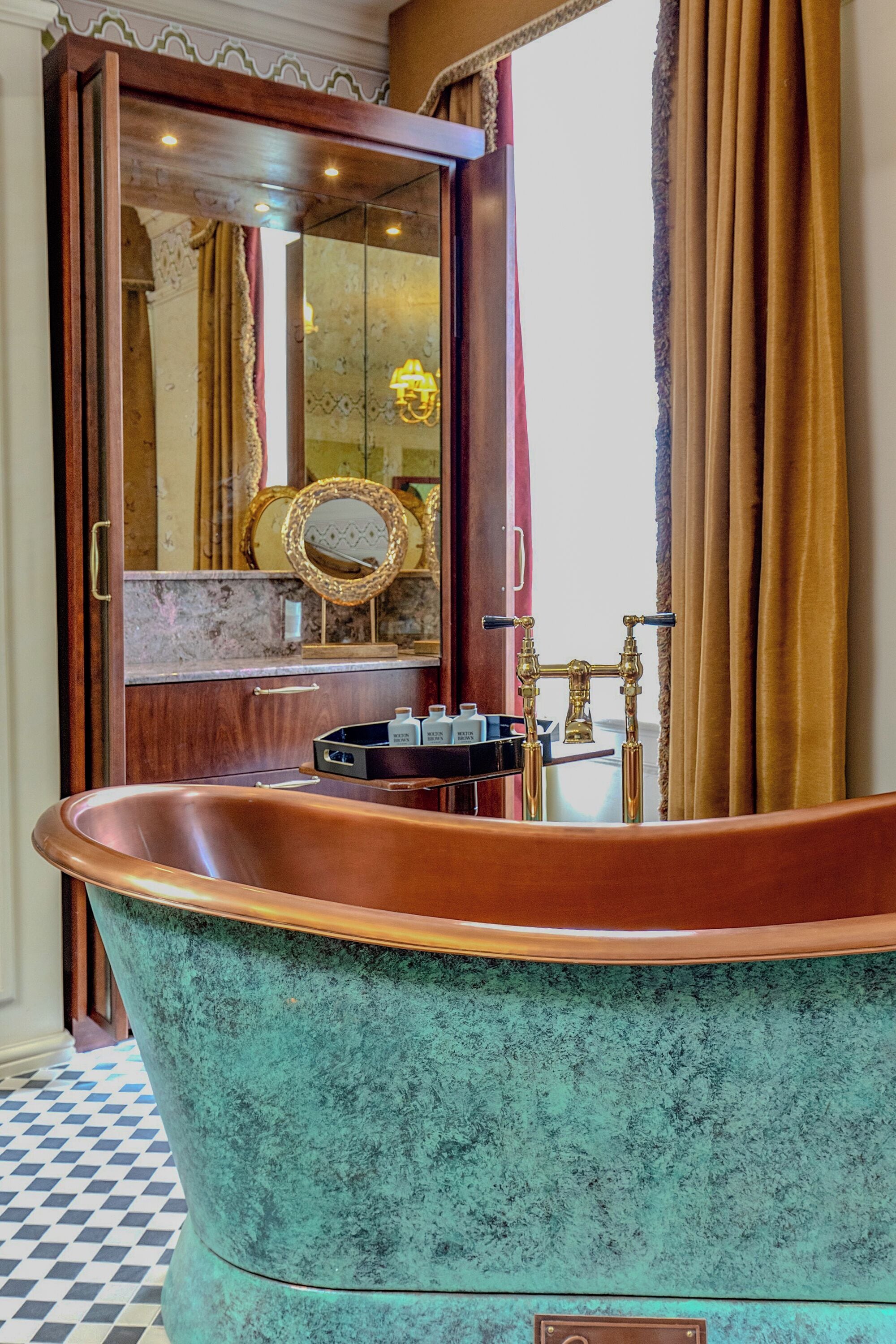 Un baño de estilo vintage con una bañera independiente, un espejo y un tocador con grifo dorado.
