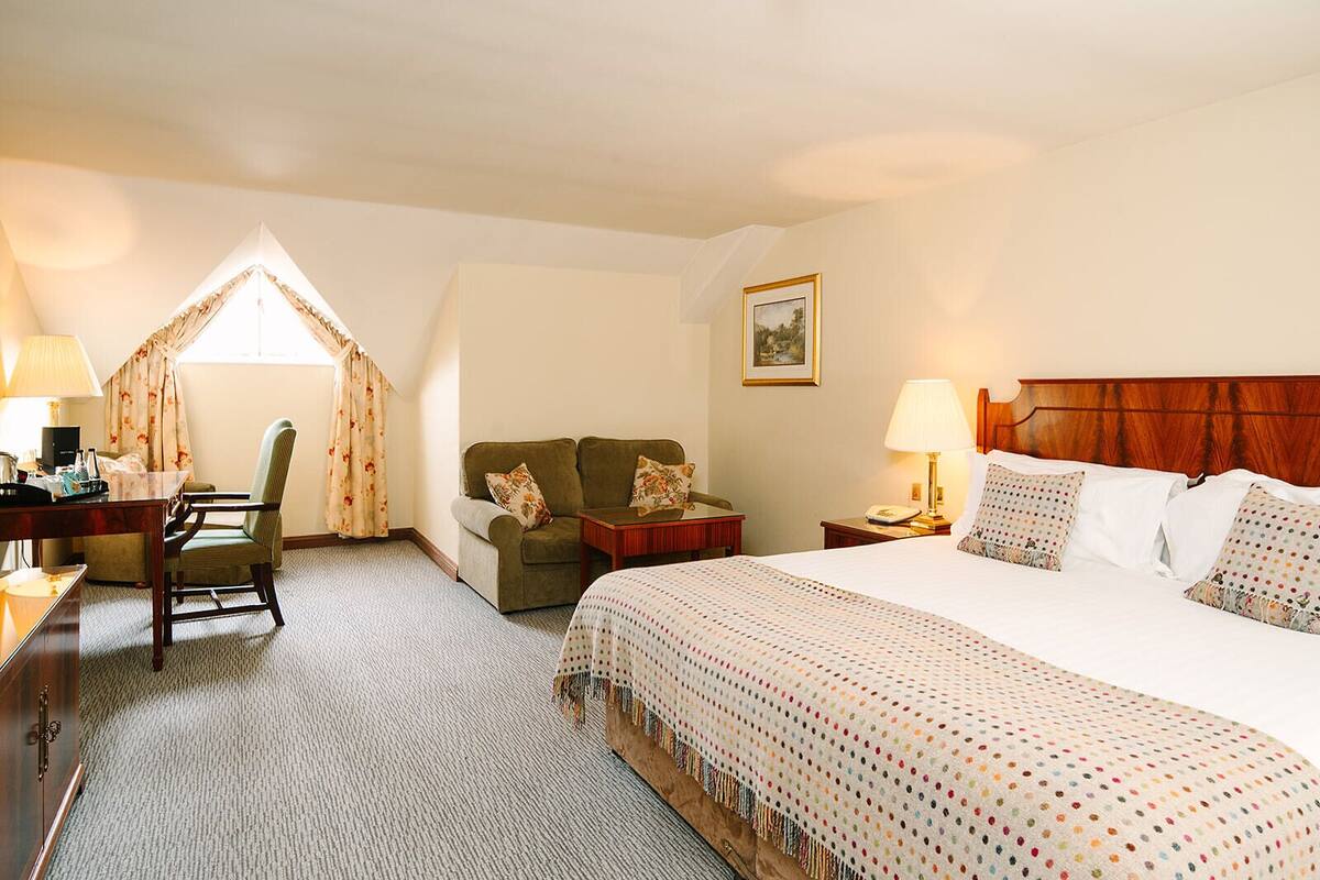 Una habitación de hotel con una cama grande, un escritorio con lámpara, una silla y un sofá.