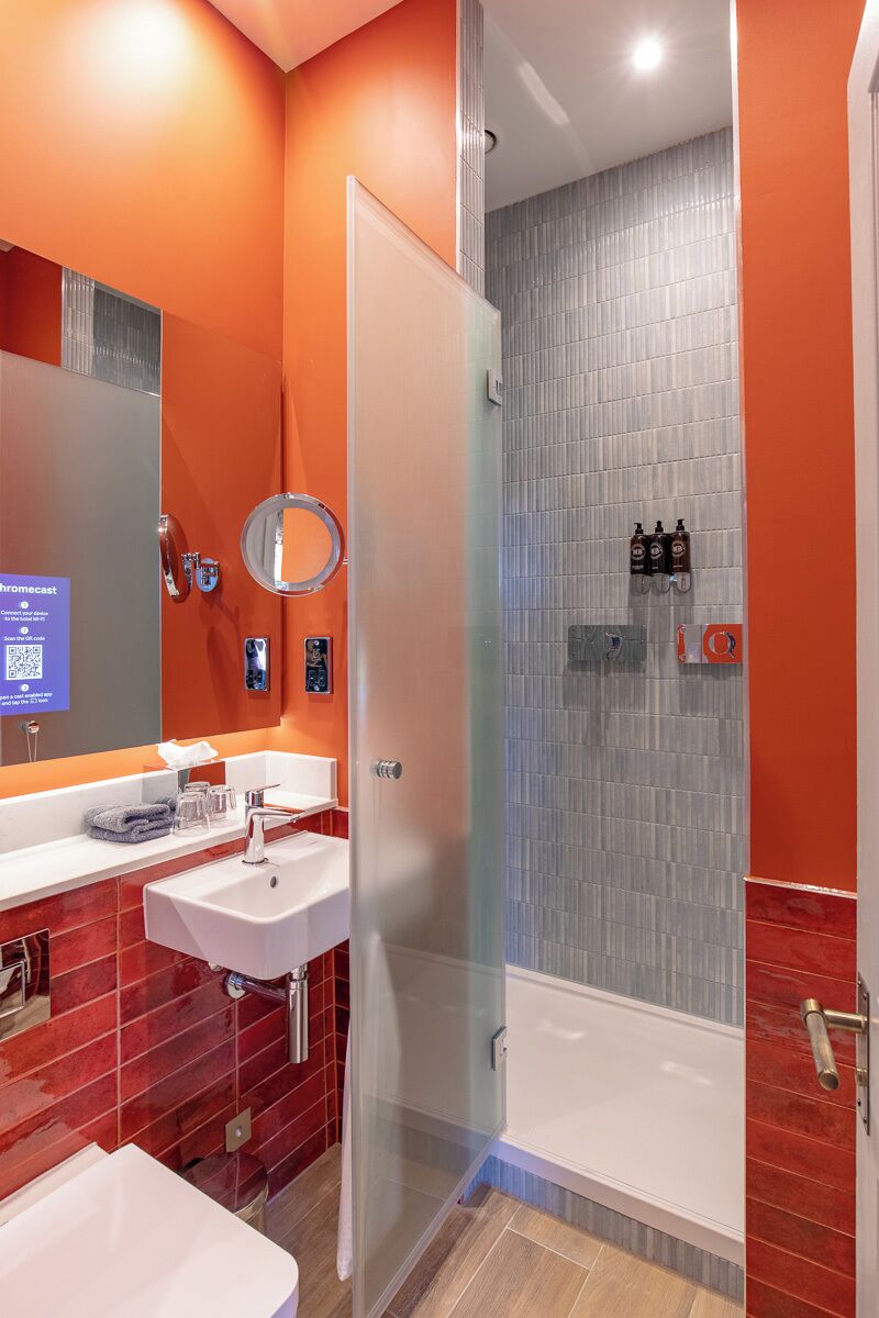 Ein modernes Badezimmer mit einer Duschkabine aus Glas, einem weißen Waschbecken und roten Fliesenwänden.