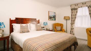 Habitación de hotel con una cama de madera, un sillón amarillo, una mesita de noche, una lámpara y un cuadro en la pared.