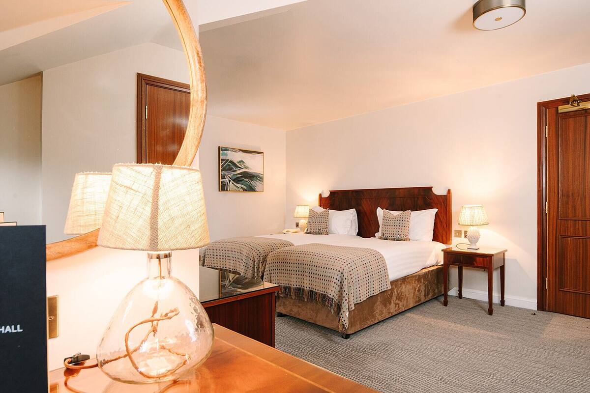 Habitación de hotel con una cama grande, dos mesitas de noche con lámparas, un cabecero de madera, un espejo y un cuadro enmarcado en la pared.