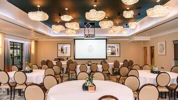 Een vergaderruimte met meerdere ronde tafels, beige stoelen en een groot scherm voor presentaties.
