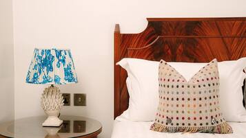 A hotel room with a wooden headboard, a round bedside table with a lamp, and a bed with white bedding and a colorful polka dot pillow.