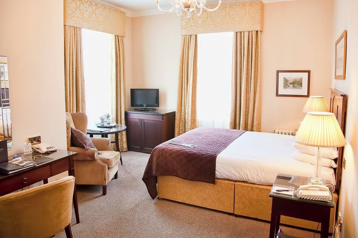 Habitación de hotel con una cama grande, un escritorio con computadora, una silla, televisor y lámpara.