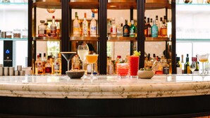 Una zona de bar con encimera de mármol, varias botellas y vasos de bebidas.